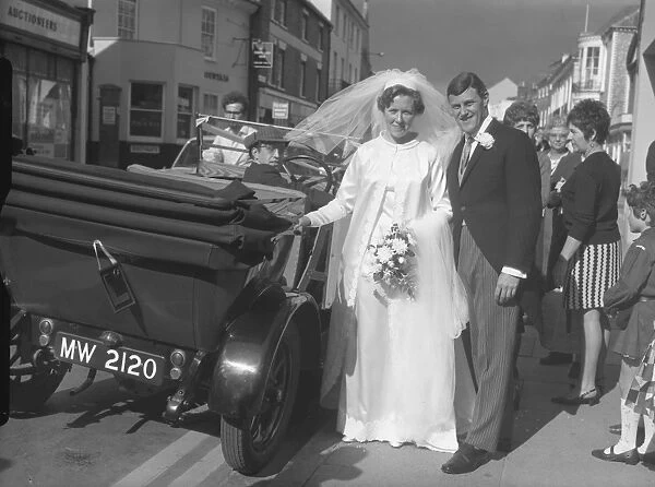 Bride and groom stood next to open top car
