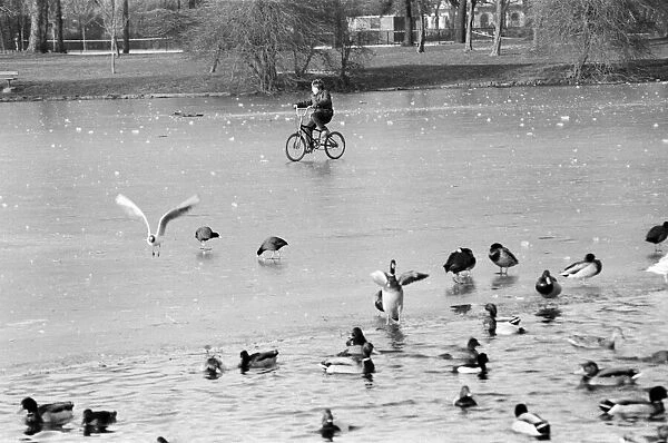 A young child riding his bike on the ice covered boating lake at Victoria Park in London
