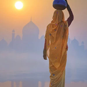 India, water carrying a water pot on a foggy morning with the sun rising on the Taj Mahal