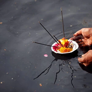 A man places an oil lamp in the polluted river Yamuna after offering prayers
