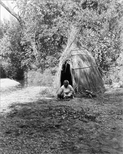 POMO COOK, c1924. A Pomo woman cooking acorns in front of a tepee made of cane