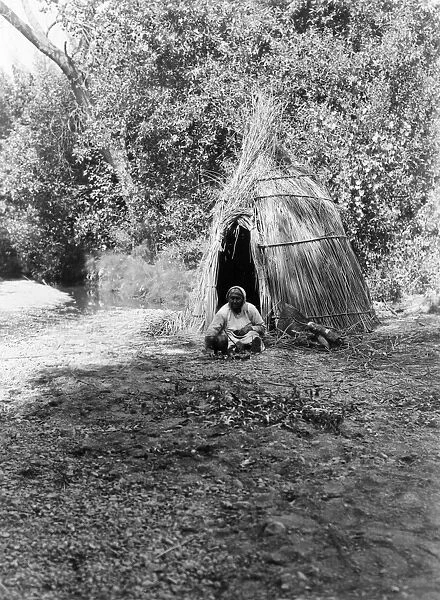 POMO COOK, c1924. A Pomo woman cooking acorns in front of a tepee made of cane