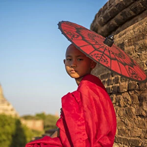 Bagan, Mandalay region, Myanmar (Burma). A young monk with red umbrella watching in