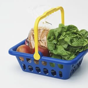 Blue basket with yellow handle, containing red apples, sliced bread wrapped in plastic and head of lettuce