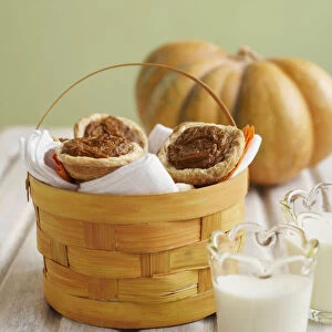 Small pumpkin pies in basket near two glasses of milk and pumpkin in background